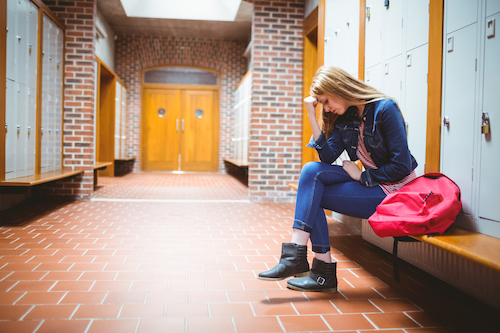 An anxious high school student sits by her locker